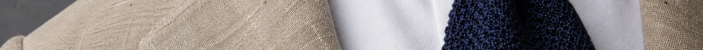Close-up cover photo demonstrating menswear texture contrast with a textured tan linen blazer, a crisp white cotton shirt, and a woven navy blue grenadine silk tie.