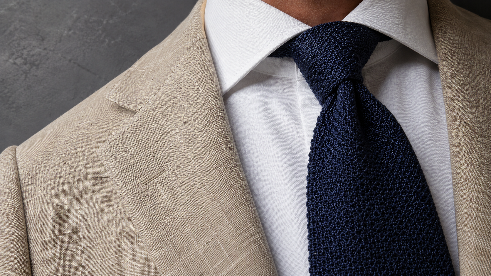 Close-up cover photo demonstrating menswear texture contrast with a textured tan linen blazer, a crisp white cotton shirt, and a woven navy blue grenadine silk tie.
